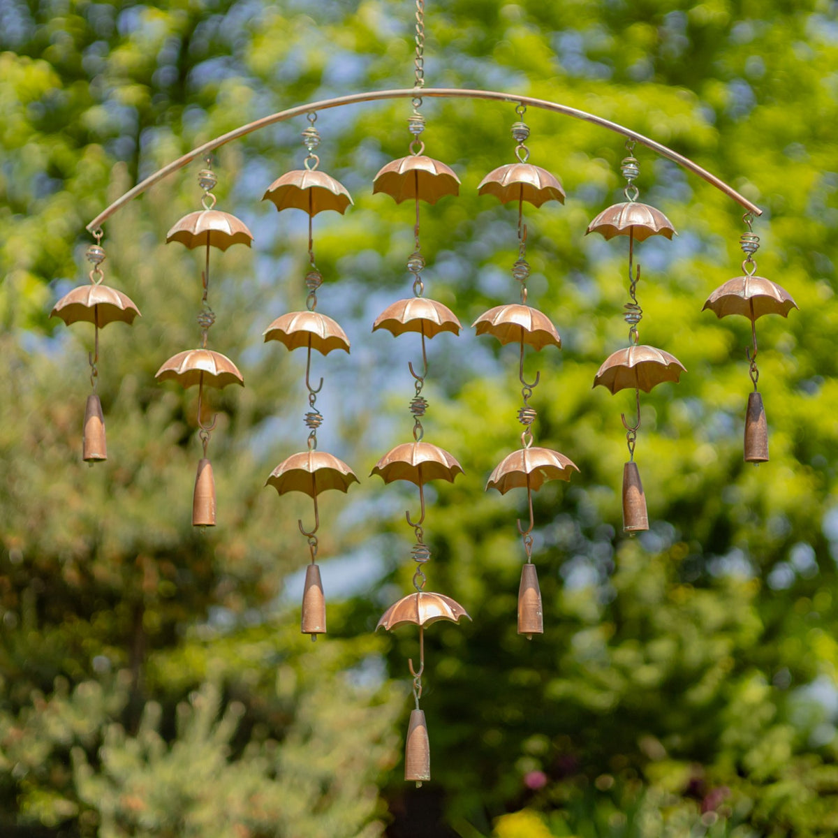 Antique copper umbrella wind chime hanging against leafy green trees