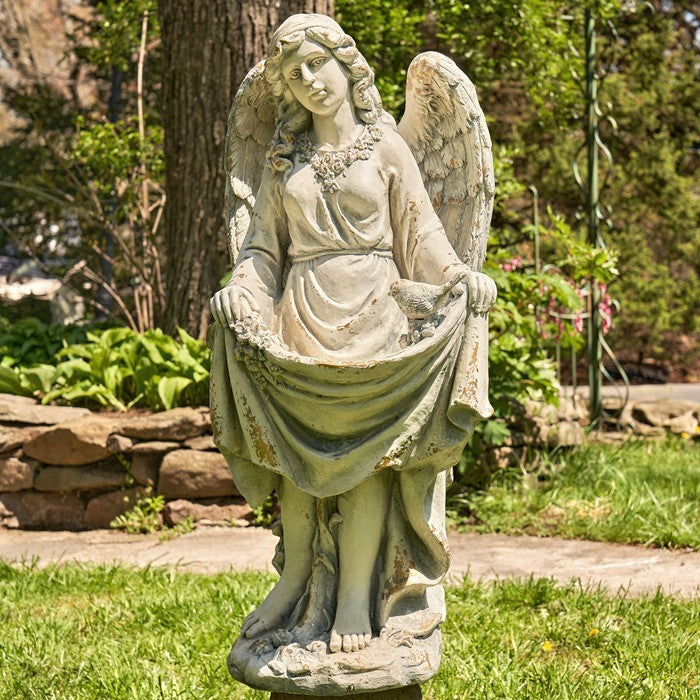 A pale-toned winged statue stands outdoors, gathering the sides of her flowing dress.