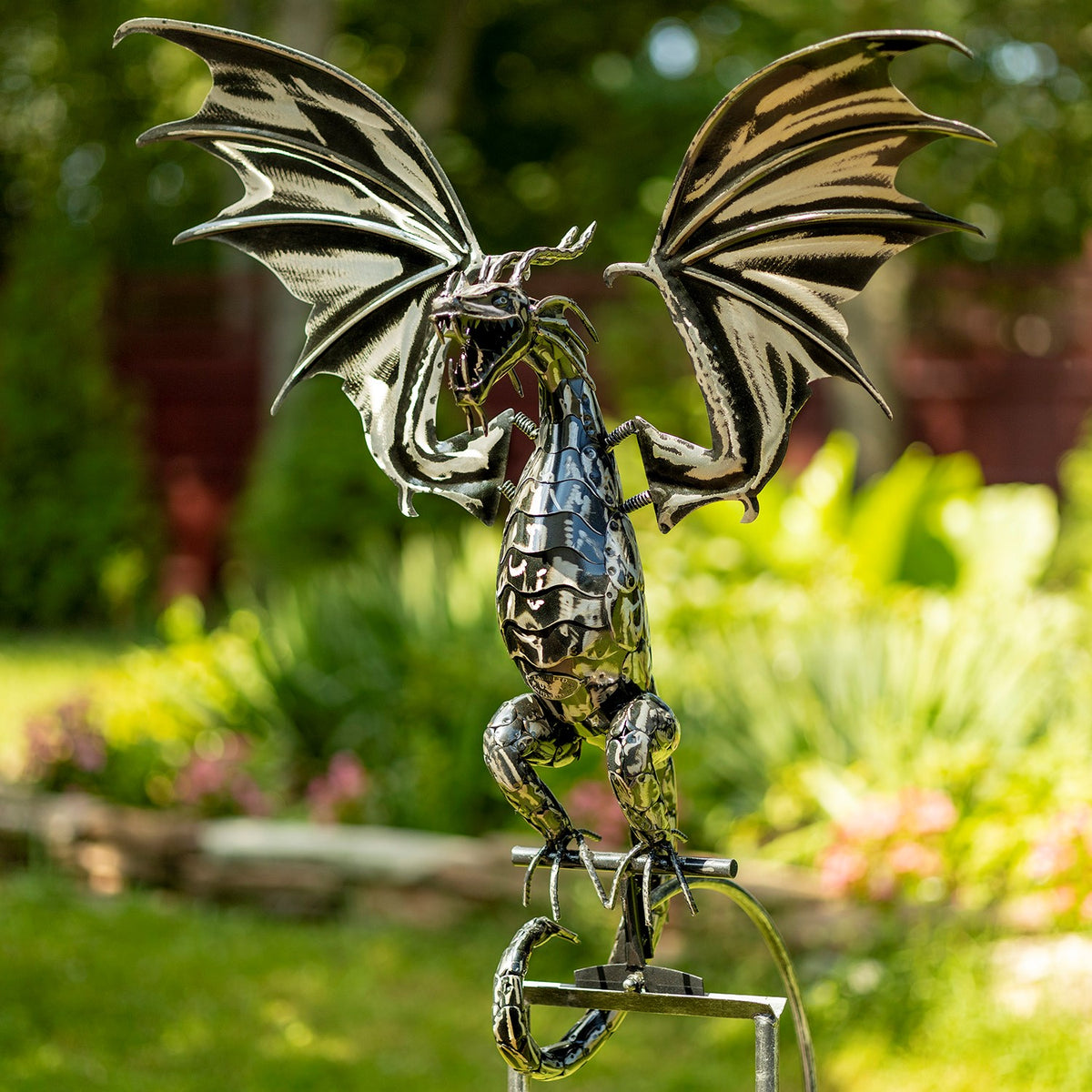 Metal dragon with spread wings perched on a garden swing stake amid greenery.