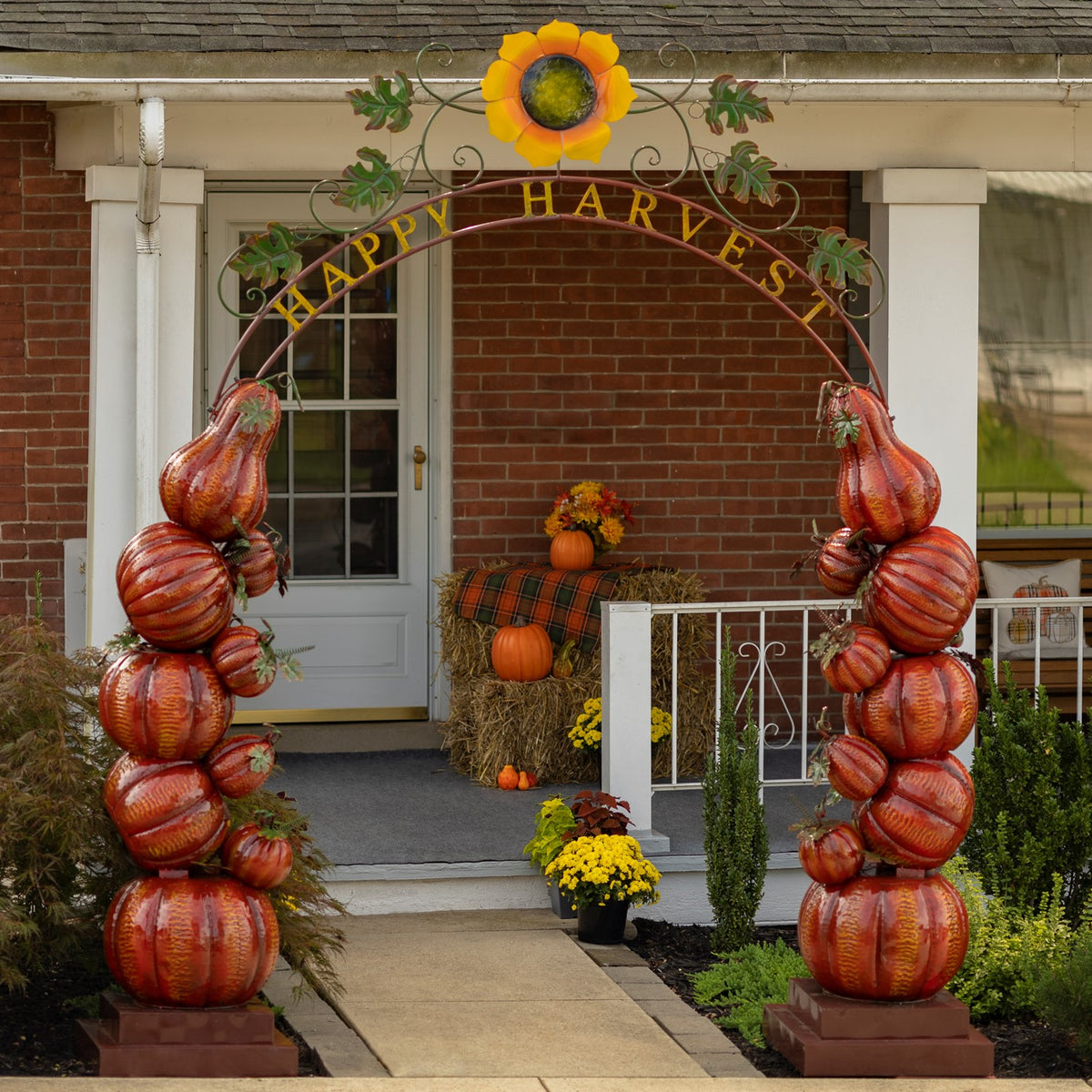 Decorative pumpkin-column arch frames a front walkway, with a sunflower and curling metalwork above.