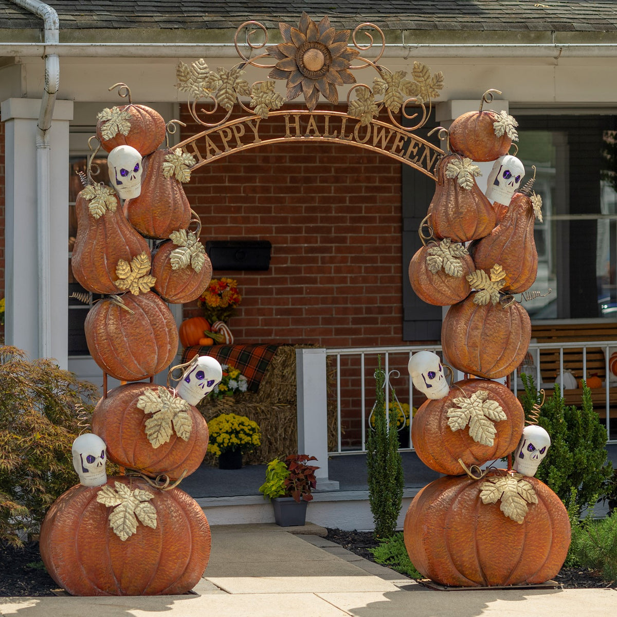 A tall pumpkin-and-skull Halloween arch frames the front entrance of a brick house.