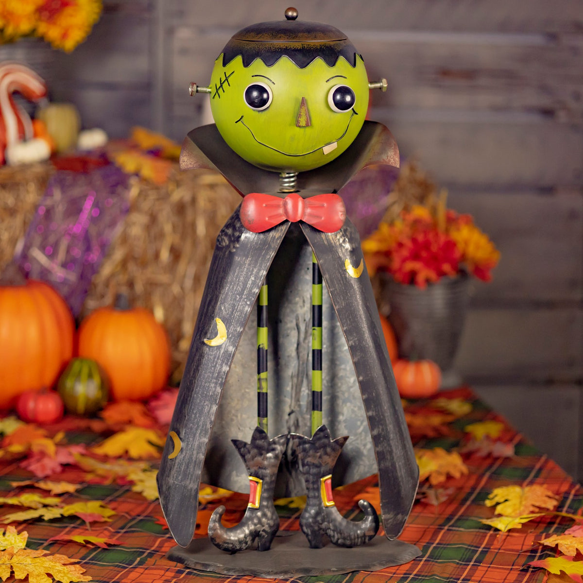 Green-headed monster figurine with dark cape, shown full-length among Halloween pumpkins