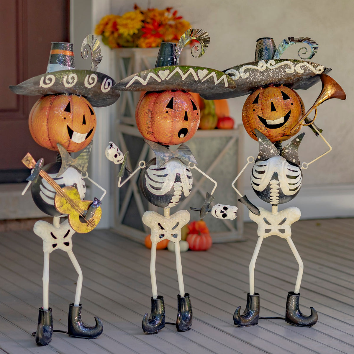 Three pumpkin-headed skeleton mariachi figurines standing together on a porch