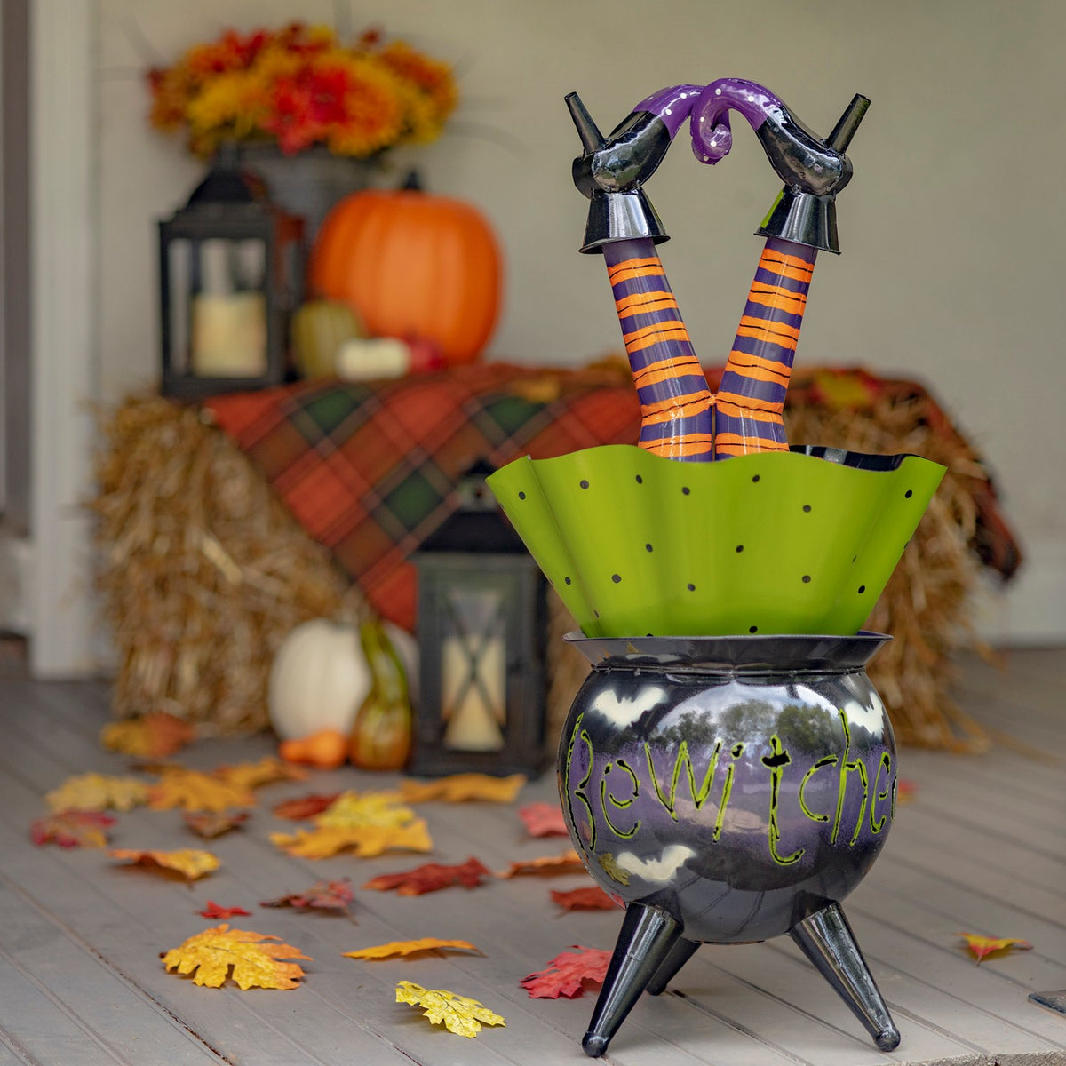 Glossy black cauldron with green skirt and witch legs in a fall porch setting