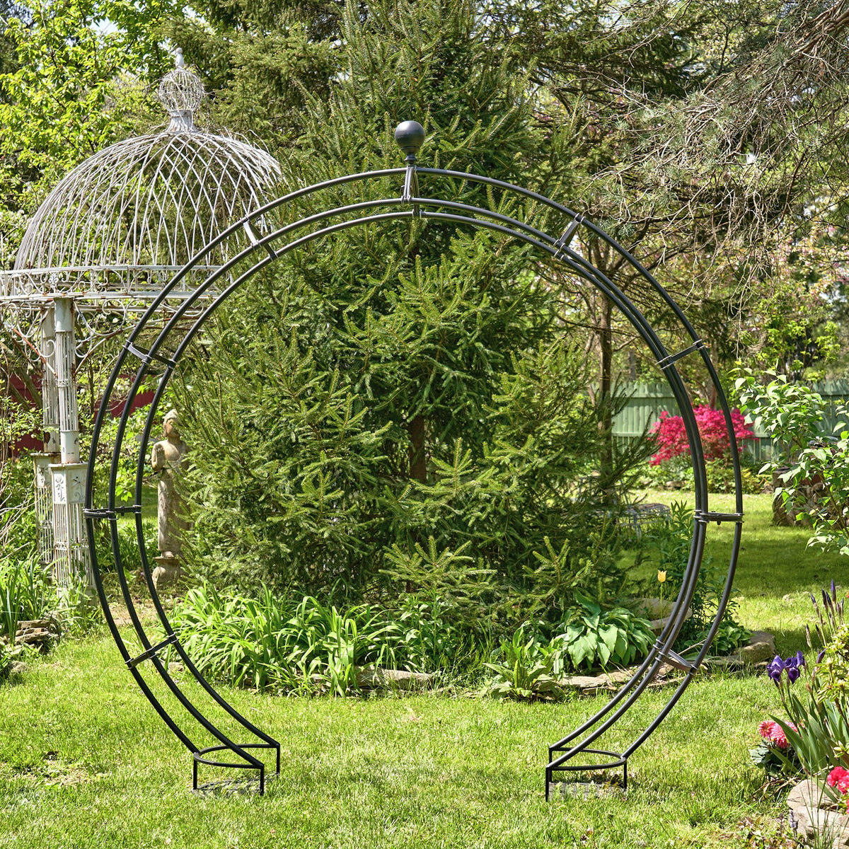 Matte black circular iron garden arch with plant stands, shown full-on in a leafy lawn
