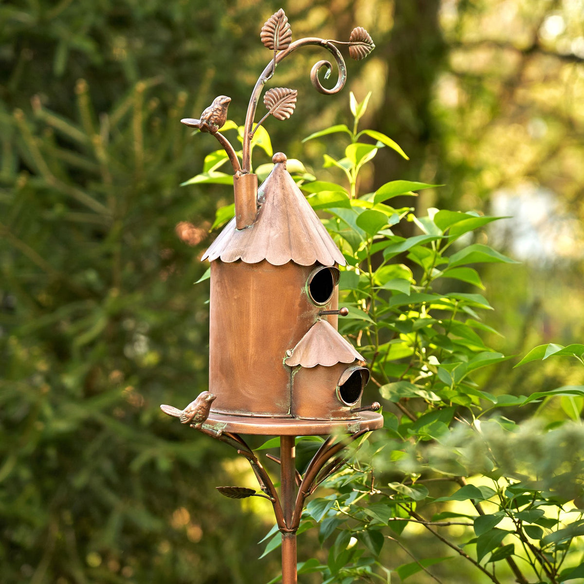 Antique copper two-story birdhouse stake among green garden foliage, front three-quarter view