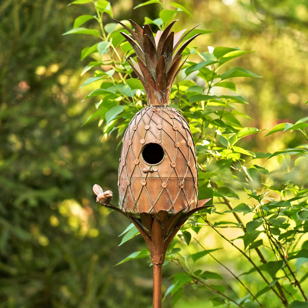 Pineapple-shaped copper-tone birdhouse stake among leafy garden plants