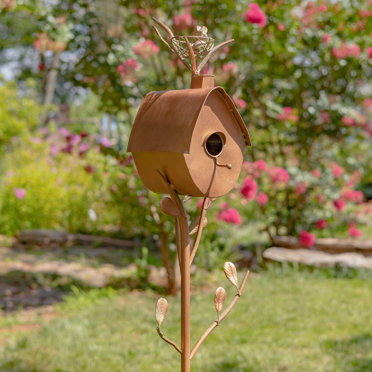 Copper-toned birdhouse with an arched roof and circular entrance, mounted on a decorative garden stake.