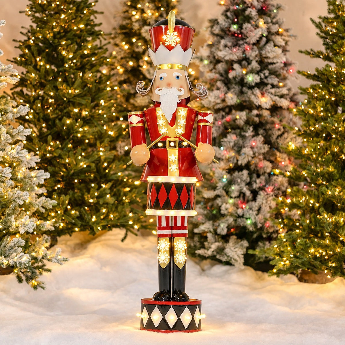 Full view of a red-and-gold nutcracker with a lit drum, standing among decorated Christmas trees.