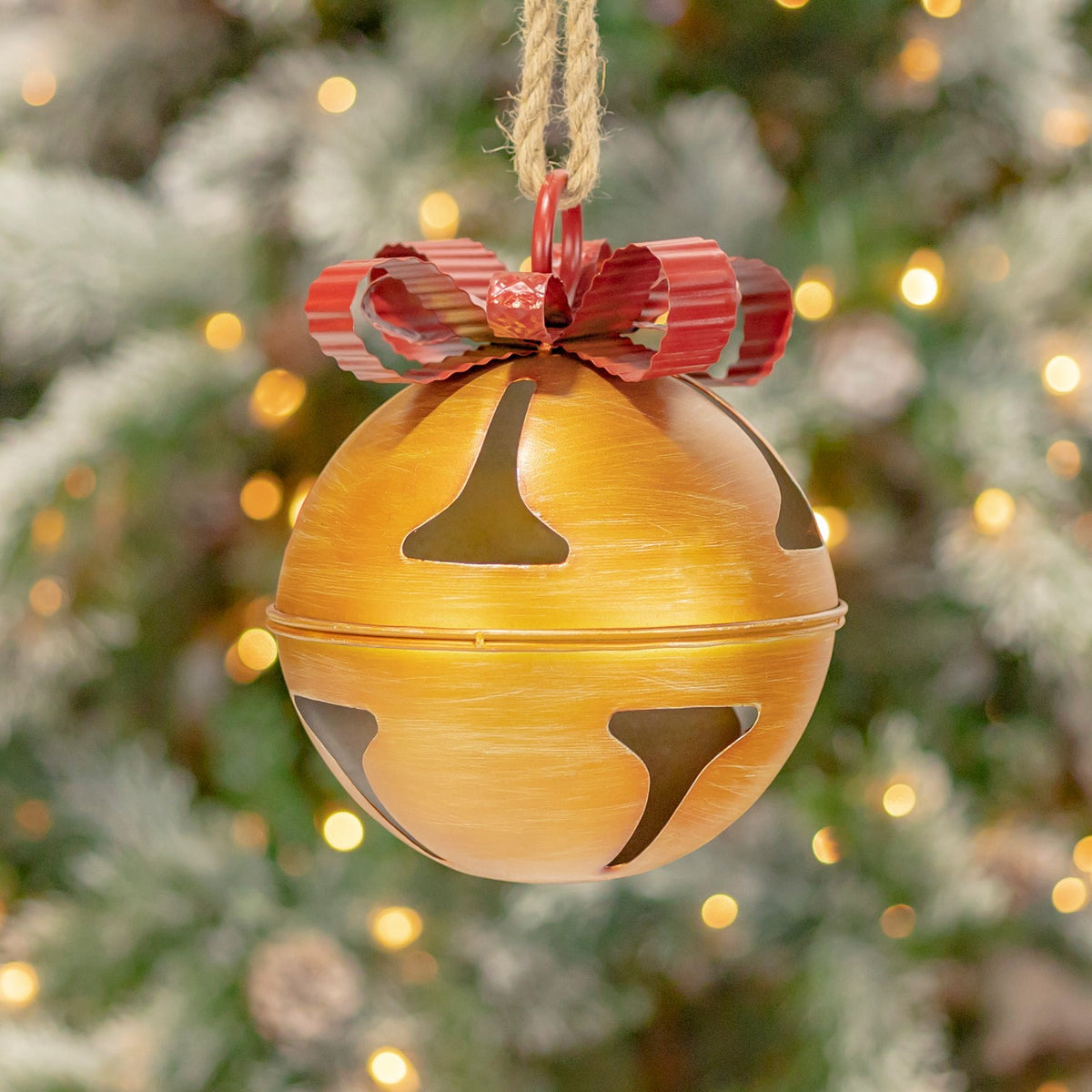 Golden hanging bell with a red bow, shown close up against holiday lights