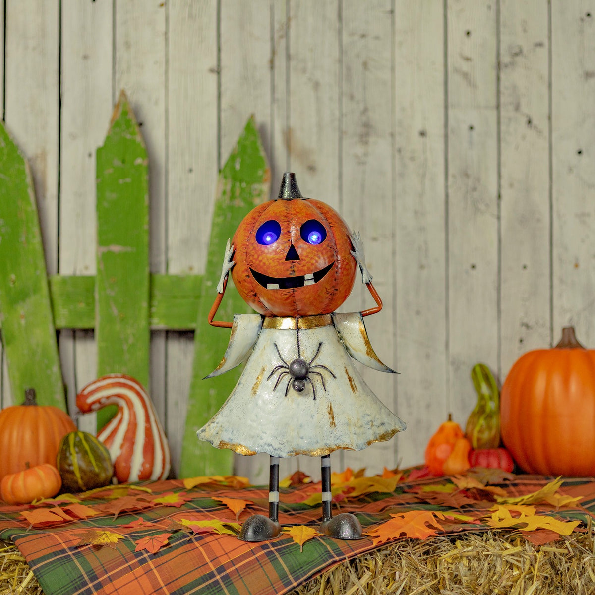 Orange pumpkin-headed ghost figurine with purple LED eyes, standing among Halloween decor