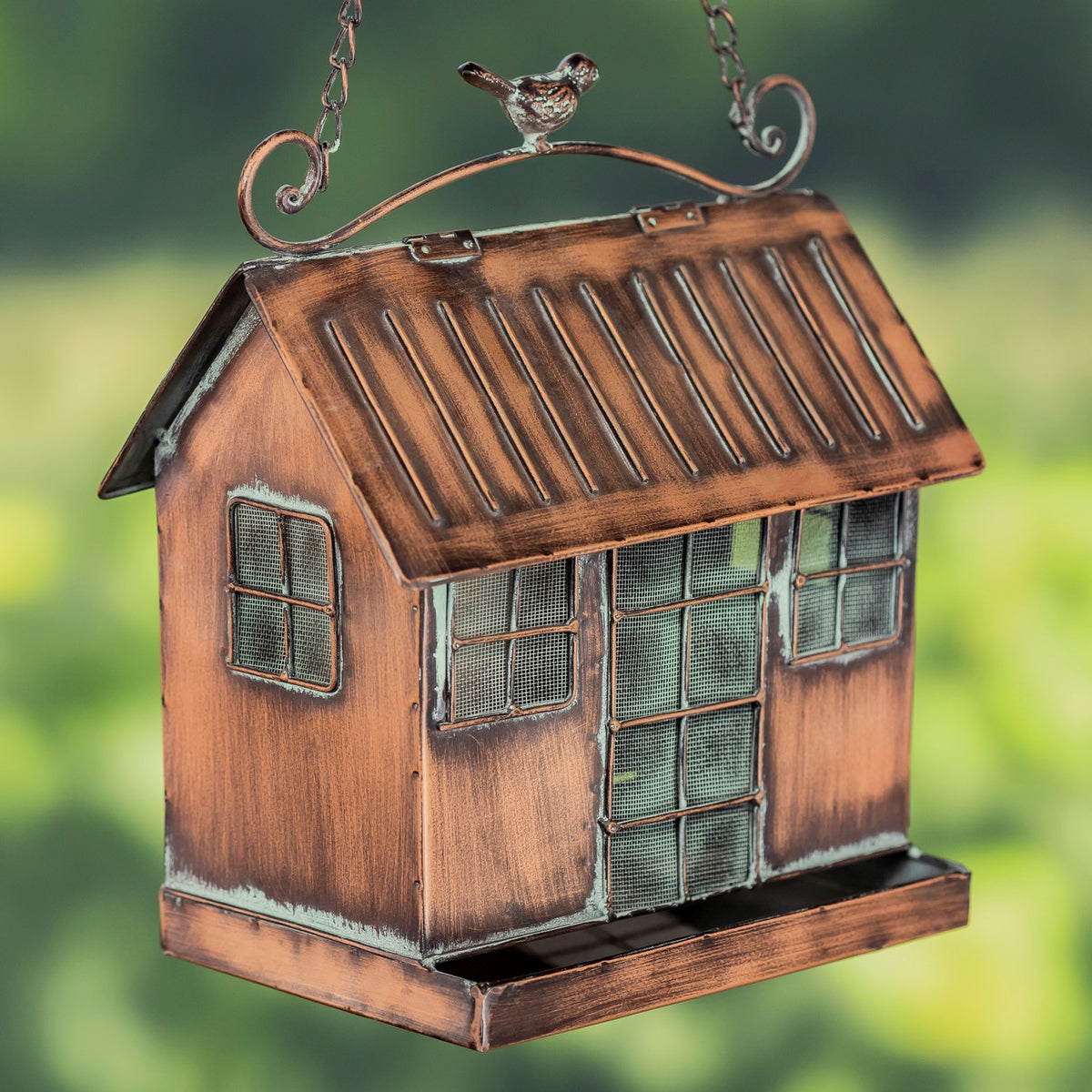 Antique copper bird feeder shaped like a small house, with mesh openings, a tray base, and a bird ornament on top.