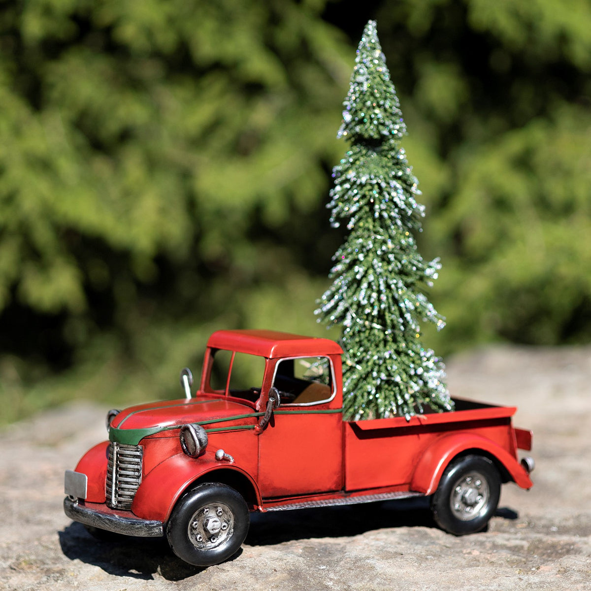 Red vintage-style pickup truck carrying a glittering Christmas tree in its bed, viewed from the front side.