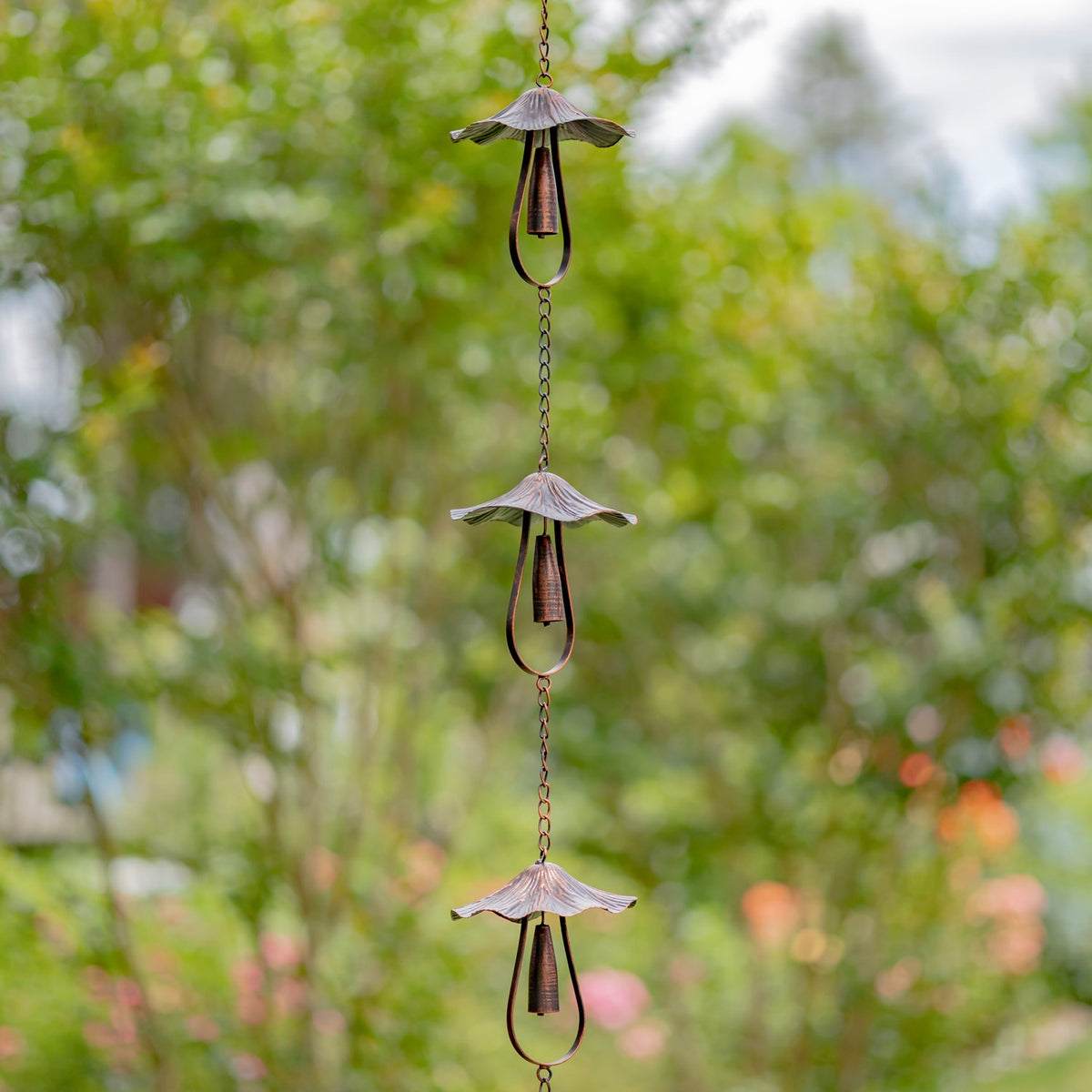Antique bronze mushroom-bell rain chain hanging vertically among green garden foliage