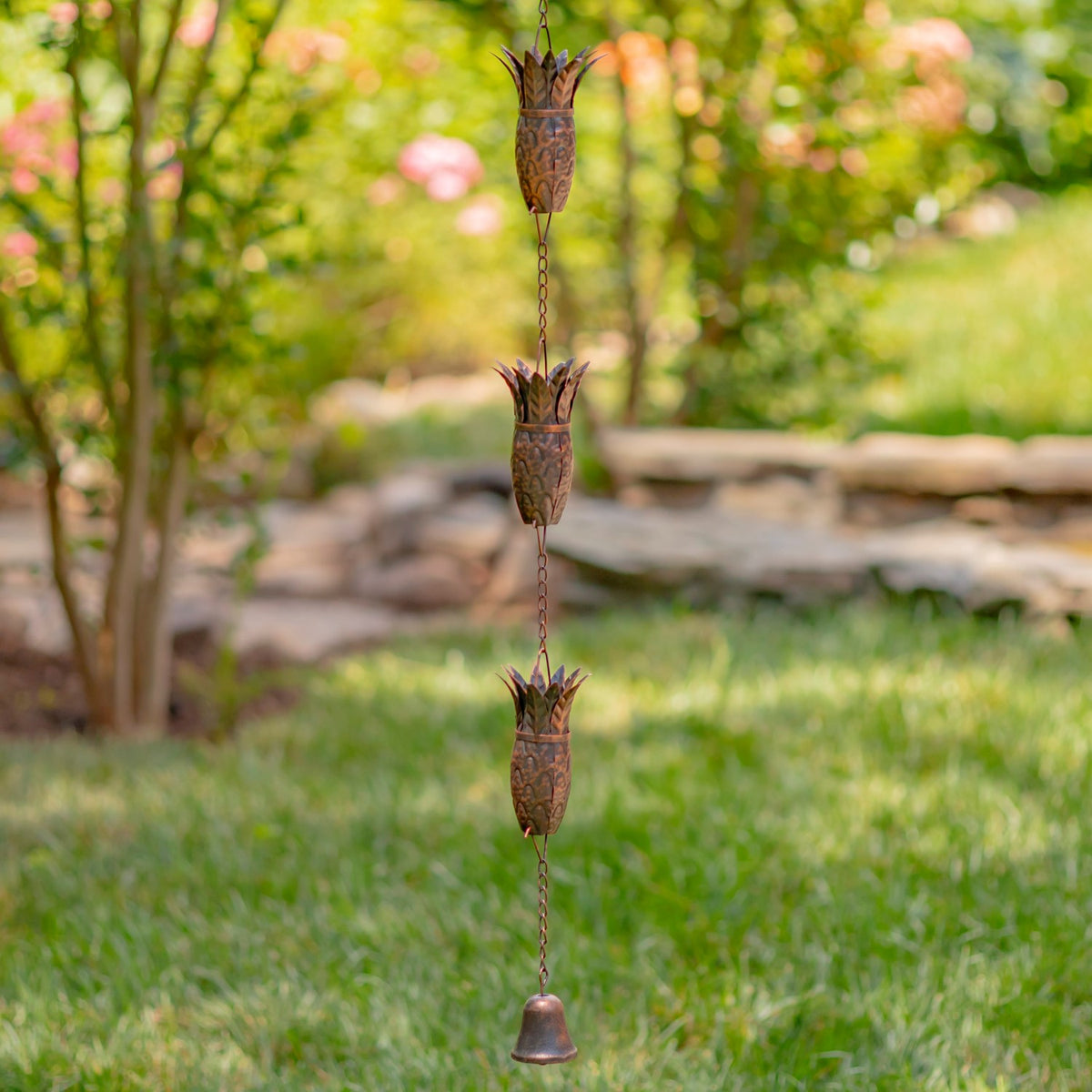 Antique bronze rain chain with pineapple-shaped links and a small bell in a garden