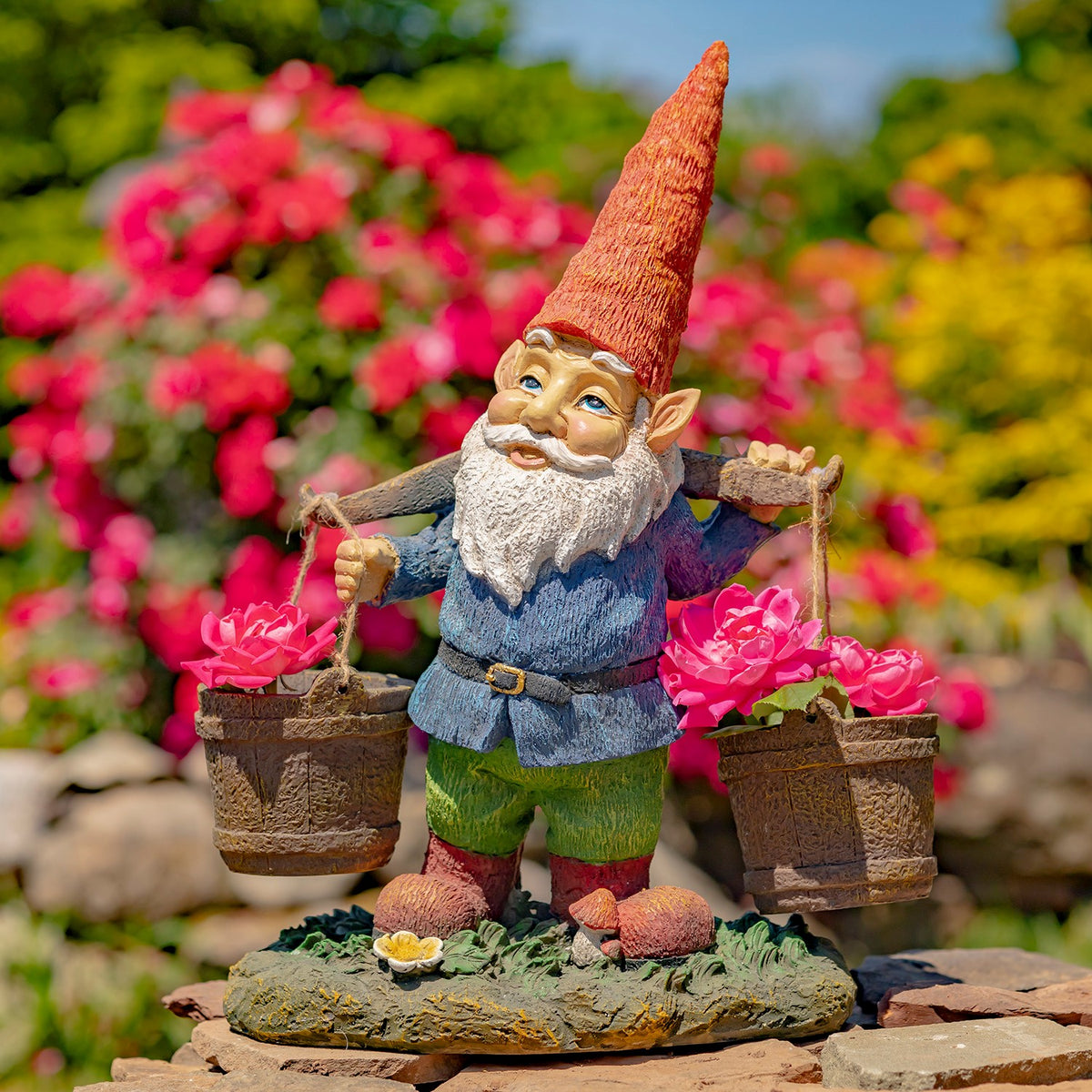 Bearded garden gnome stands among flowers, holding two flower-filled buckets.
