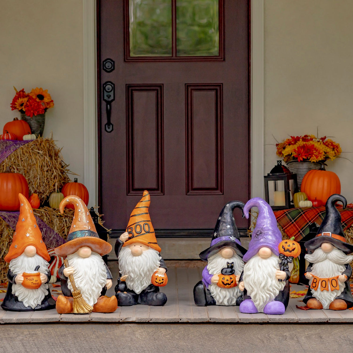 Six assorted Halloween gnome statues arranged on a porch in front of a dark door