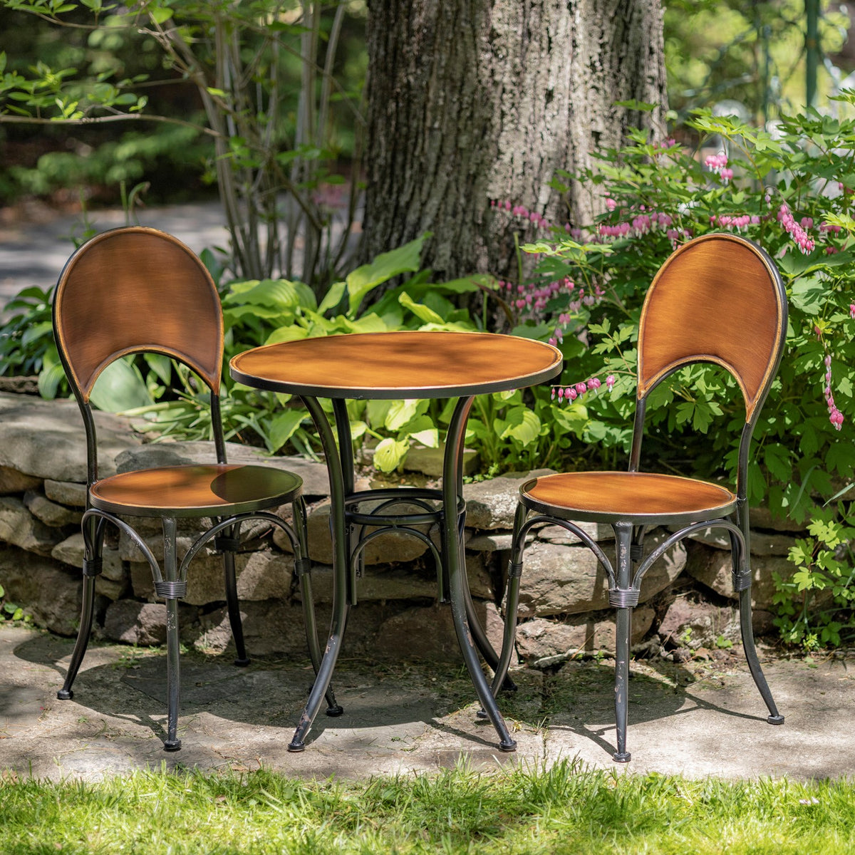 Antique copper round bistro table and two chairs outdoors among greenery