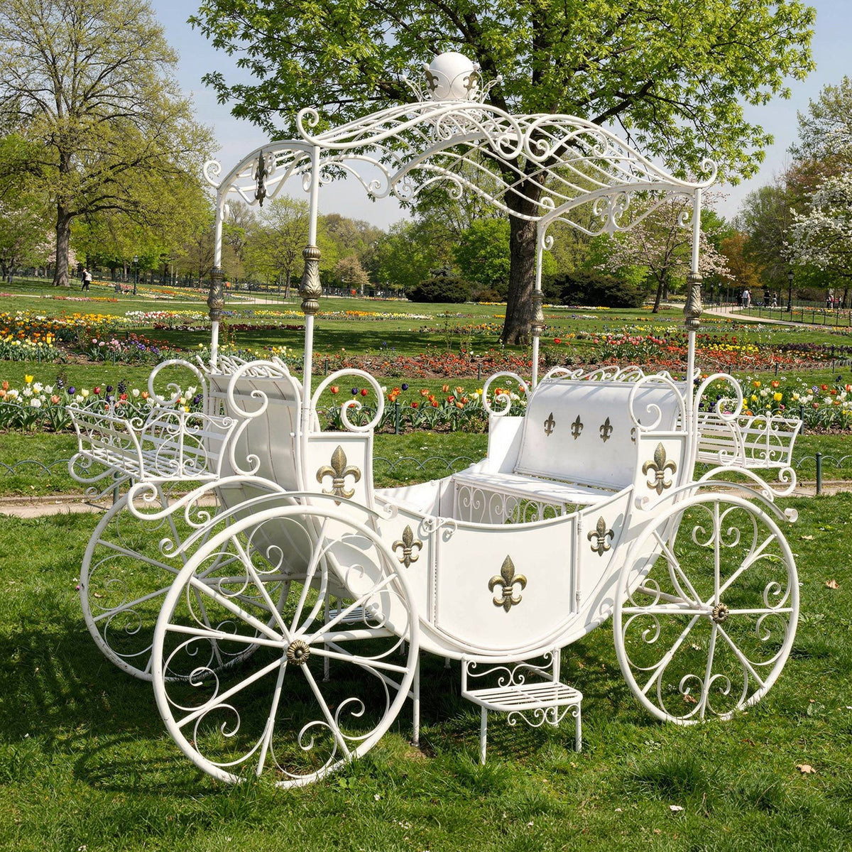 Antique white iron carriage with planters and ornate wheels on a lawn, angled front view
