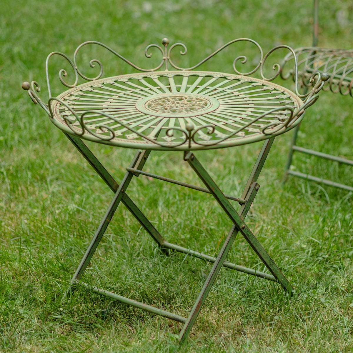 Greenish-brown folding garden table with an ornate round top, shown on a lawn.