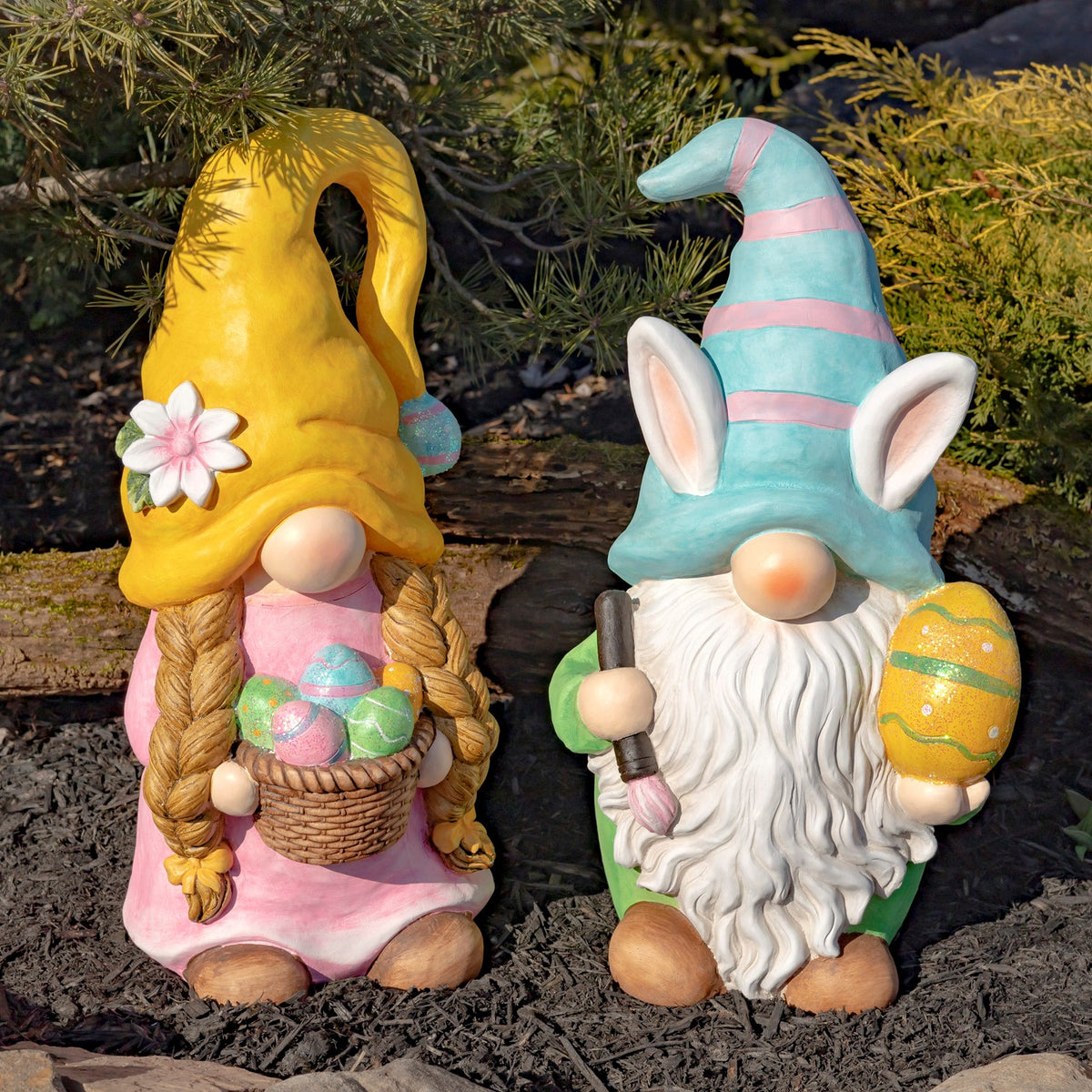 Pair of colorful Easter garden gnomes standing outdoors among mulch and evergreen shrubs