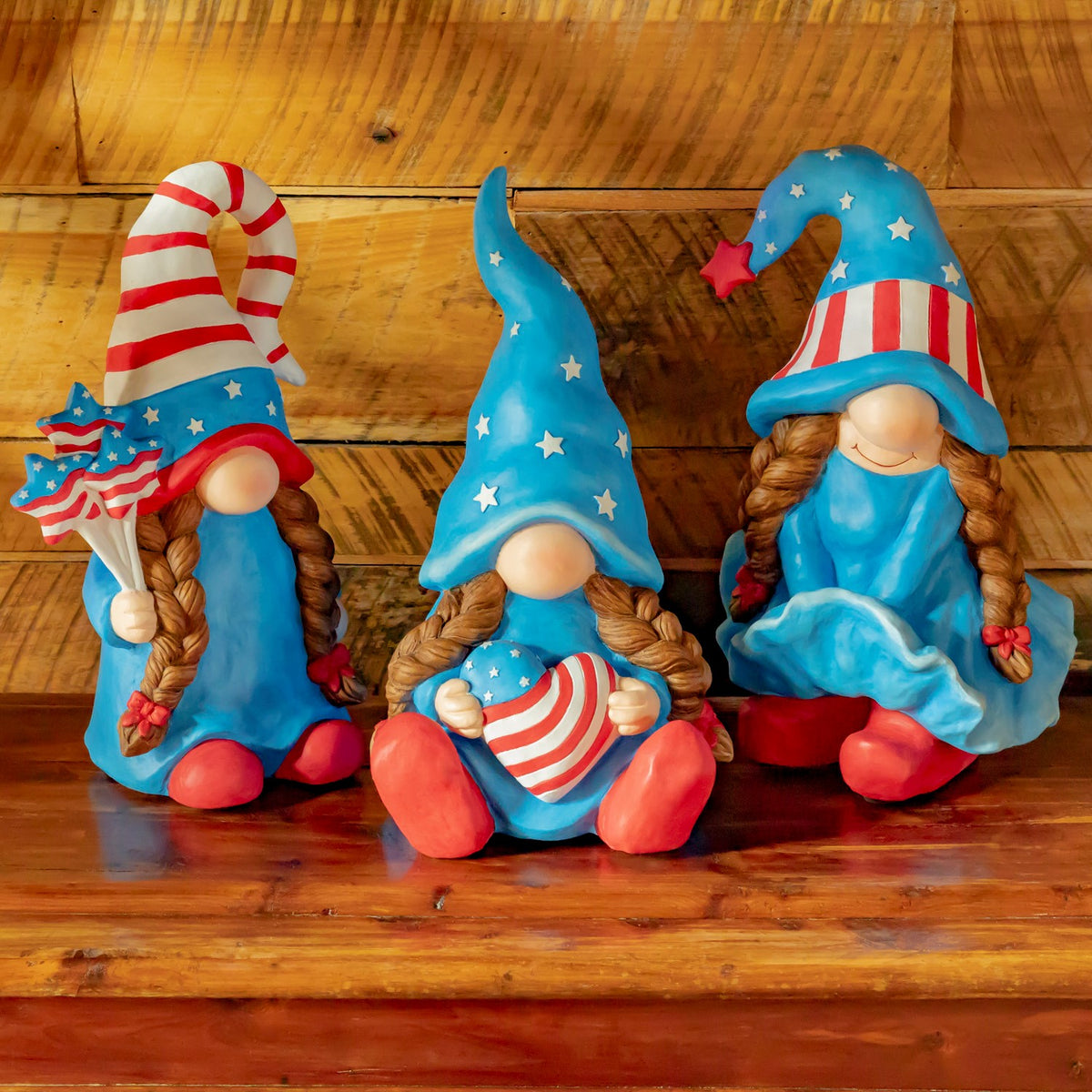 Three patriotic gnome figures sit together on a wooden surface, each wearing a blue, red, and white outfit.