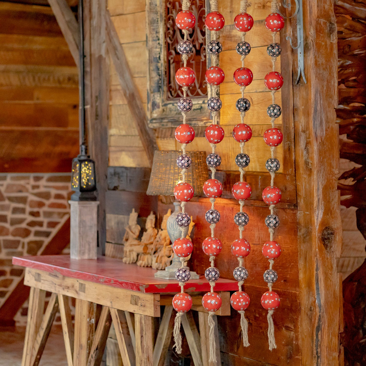 Four strands of red and patterned dark porcelain balls hang beside a rustic wooden table.