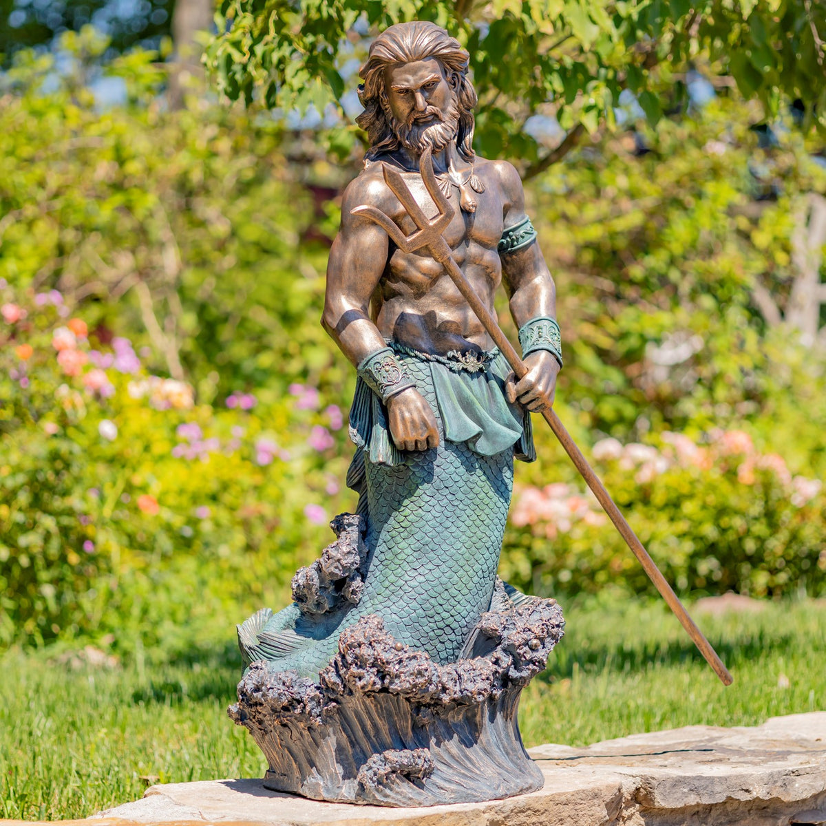 Full view of a bearded merman statue holding a trident, standing on a sculpted wave base in a garden.