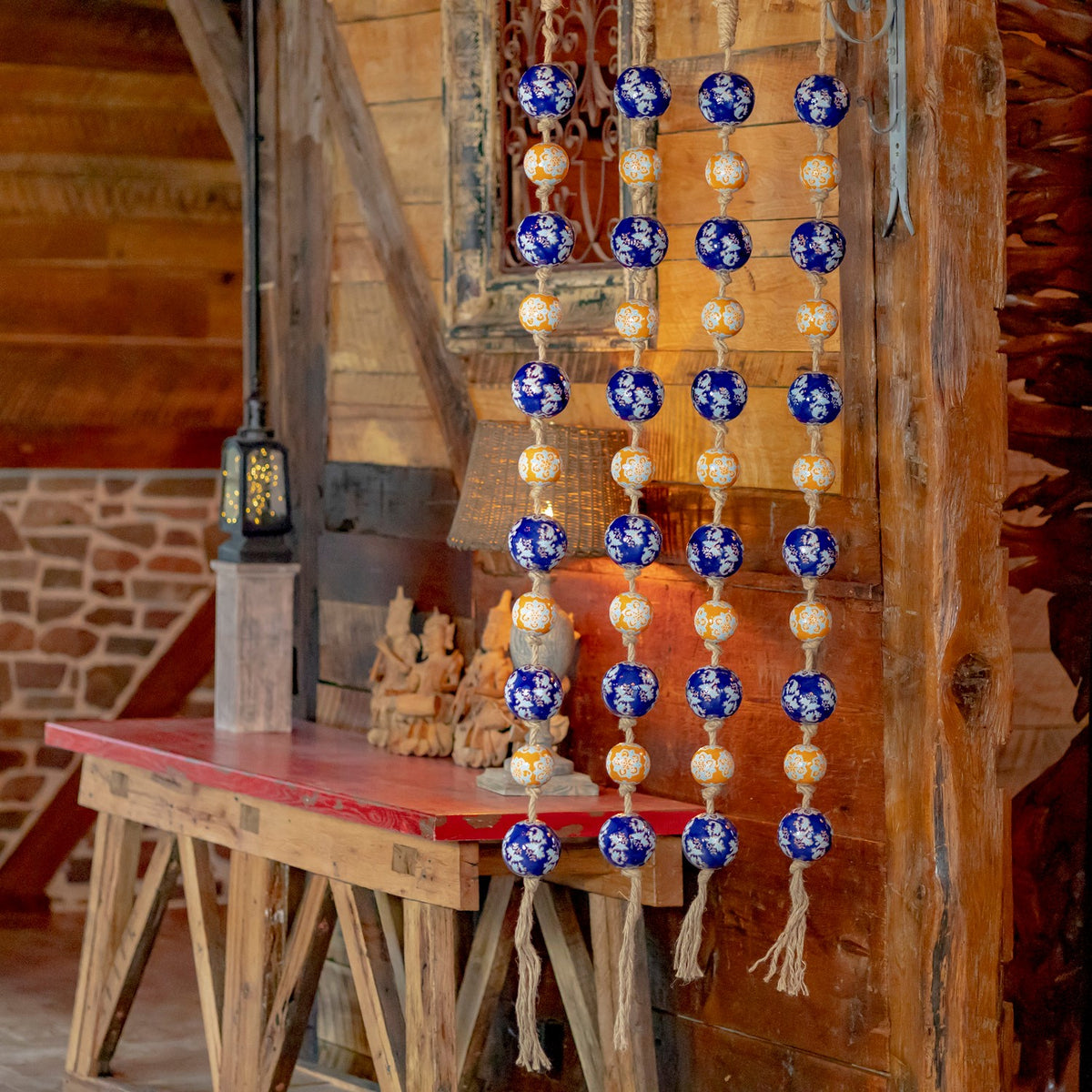 Blue and orange patterned porcelain balls hang in four strands against a rustic wooden wall.