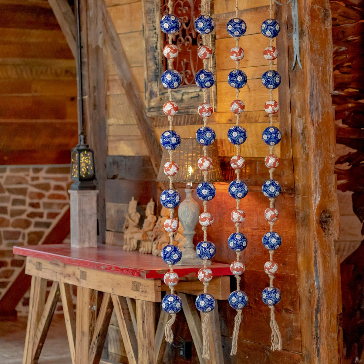 Four strands of blue and burnt-orange patterned porcelain balls hang beside a rustic wooden table.