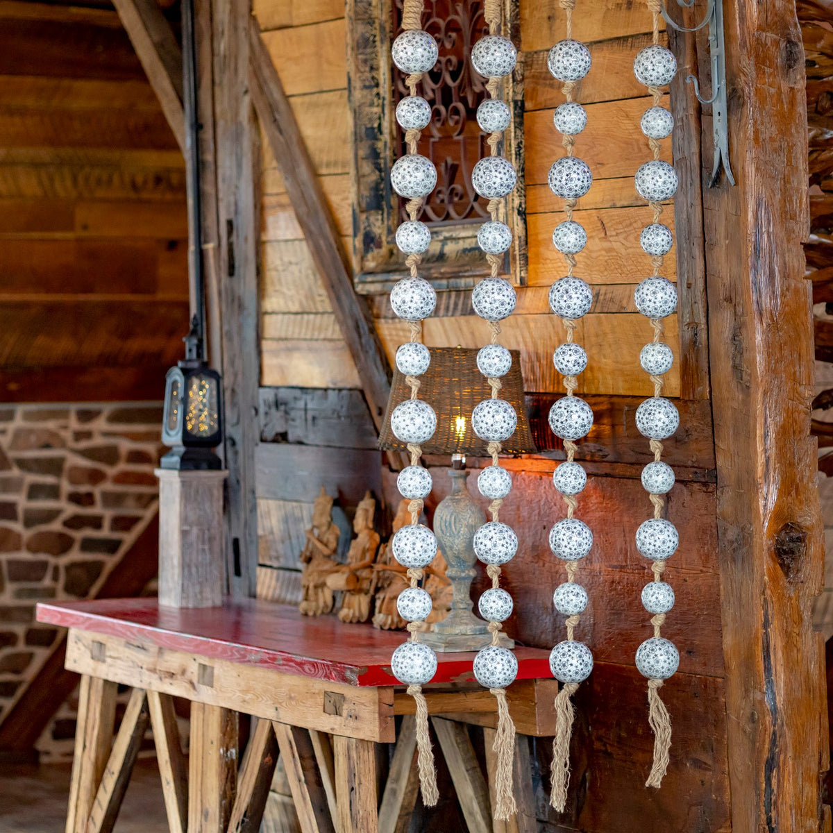 Four strands of patterned white, gray, and black porcelain balls hang against a rustic wooden wall.