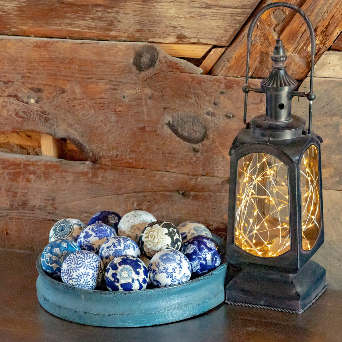 Blue-and-white patterned ceramic balls arranged in a shallow blue bowl beside a glowing lantern.