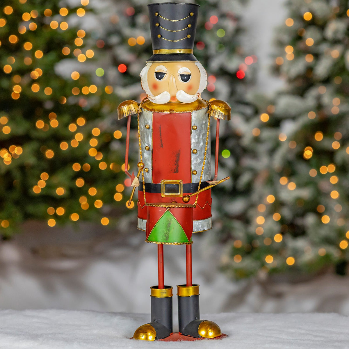 Full-length front view of a painted metal nutcracker in a snowy holiday display