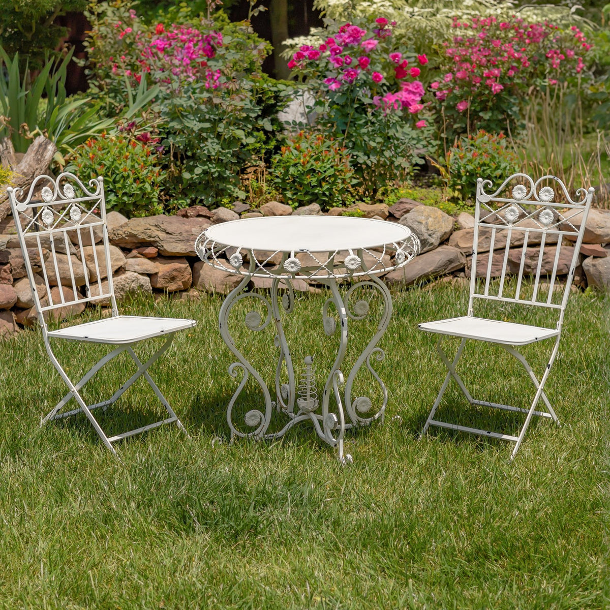 Antique white bistro table and two folding chairs on a lawn among garden flowers