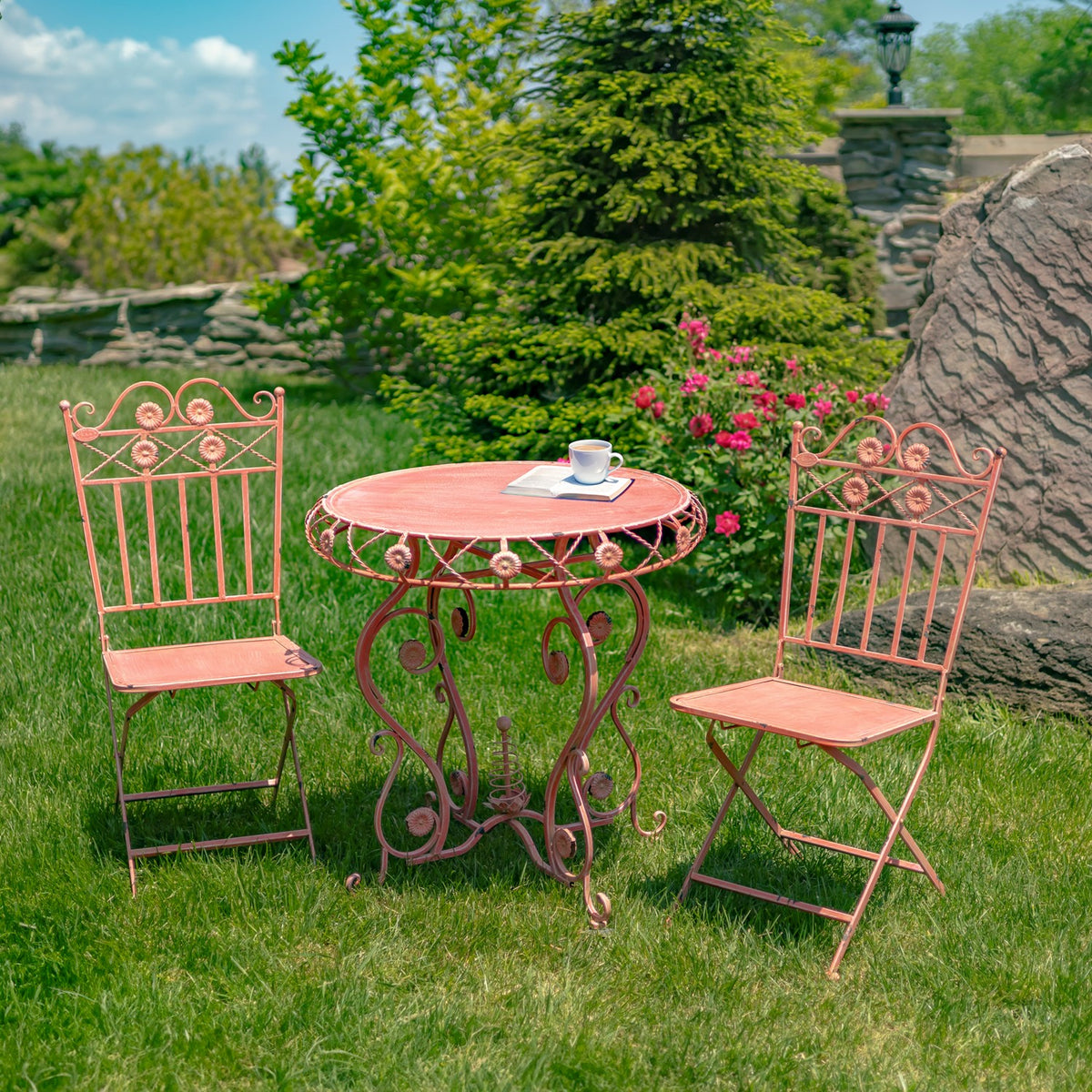 Flamingo pink bistro table and folding chairs on a lawn with a cup on the table