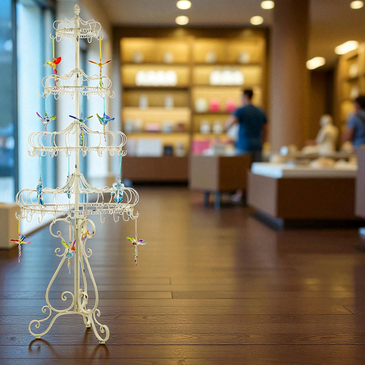 Tall ivory metal display stand with tiered circular rails and colorful hanging ornaments in a shop.