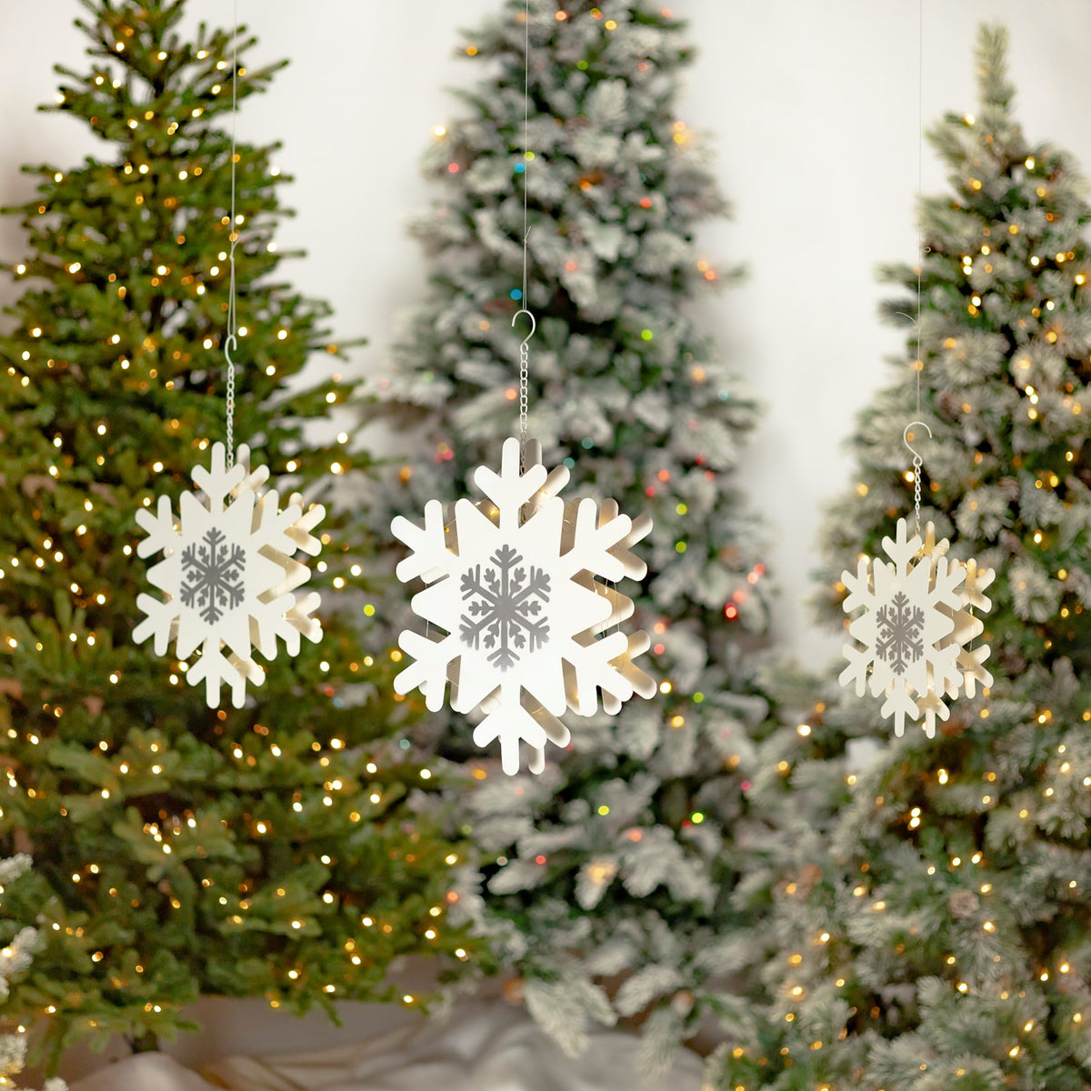 Three white and silver LED snowflakes hanging in front of decorated Christmas trees