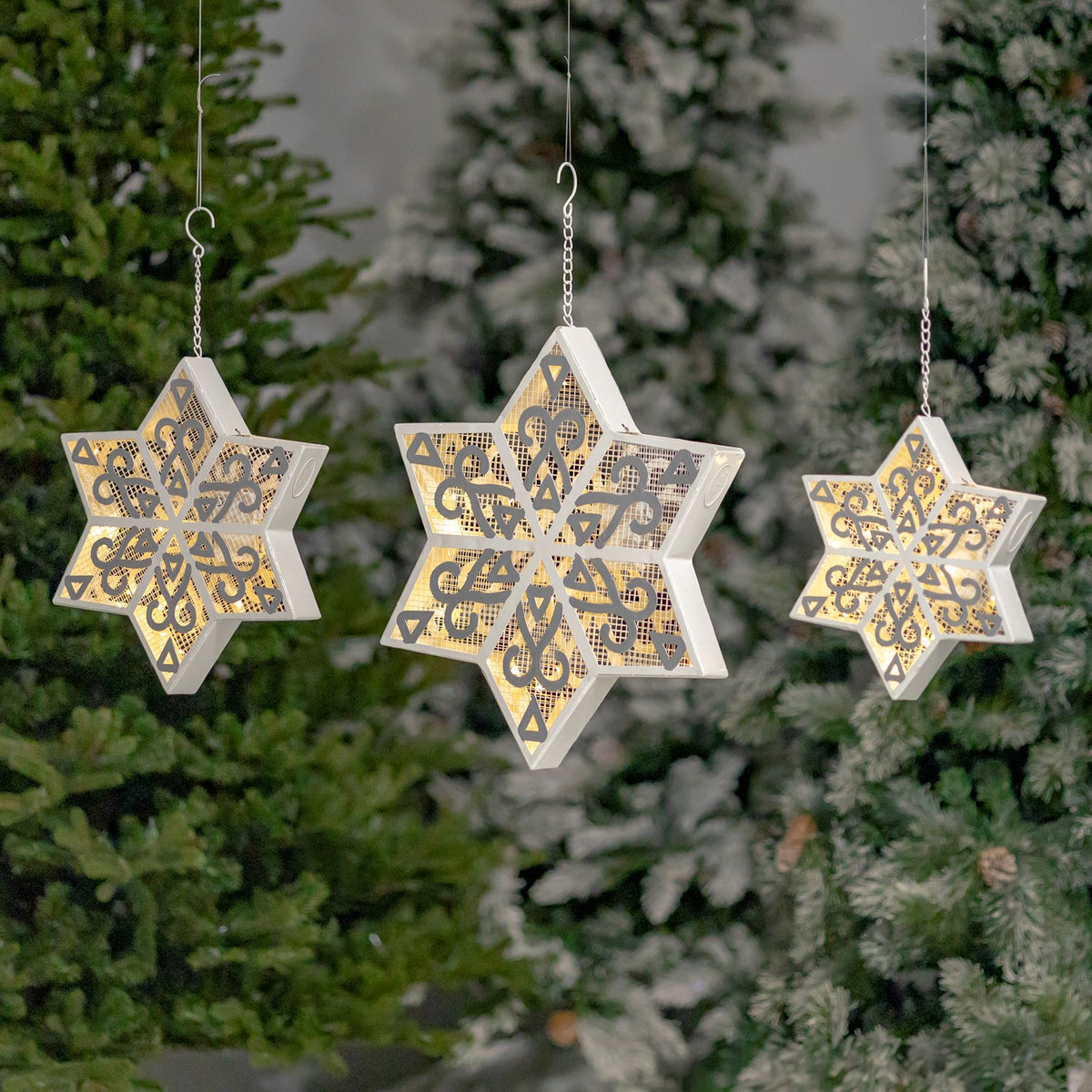 Three illuminated white and silver six-point snowflakes hanging among evergreen branches