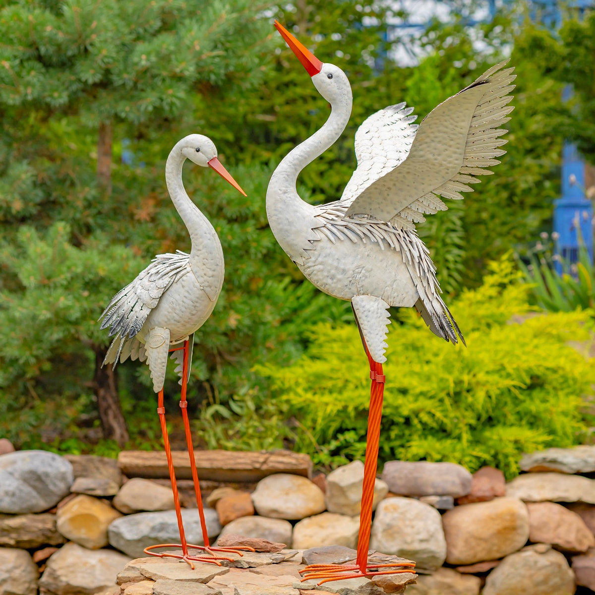 Two white heron statues stand among garden stones, one with its wings raised.