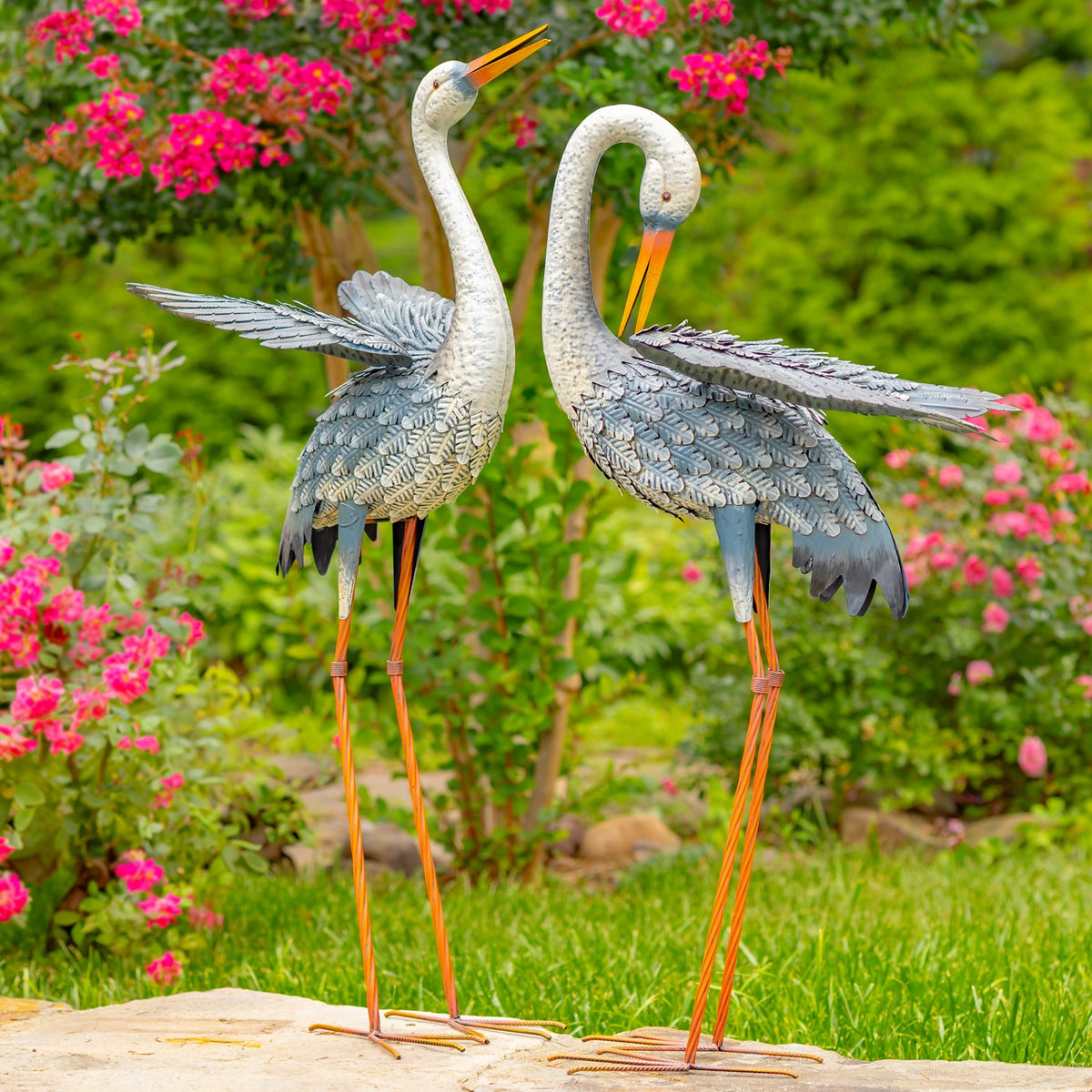 Pair of blue-and-white egret figurines standing in a flower garden