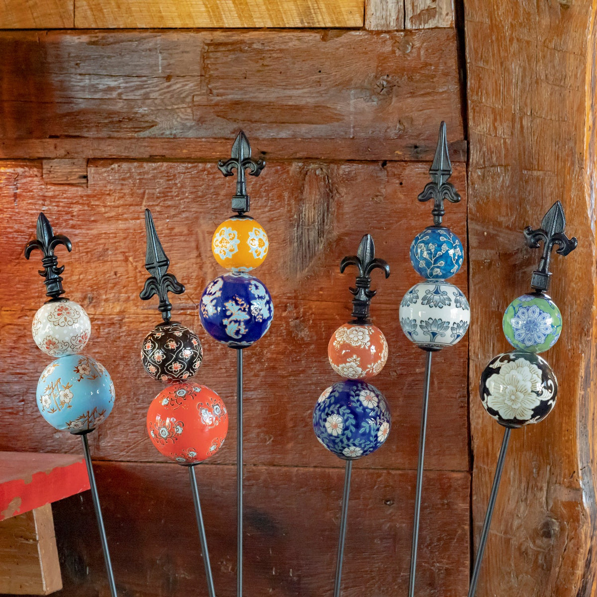 Six colorful patterned ceramic and iron garden stakes displayed against a wooden wall