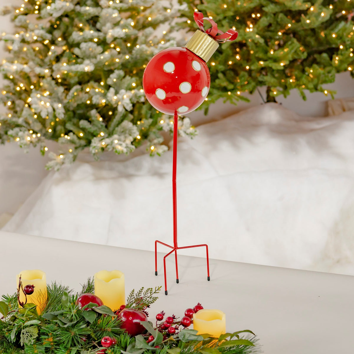 Red polka-dot ornament stake standing beside greenery and candles beneath a lit Christmas tree.