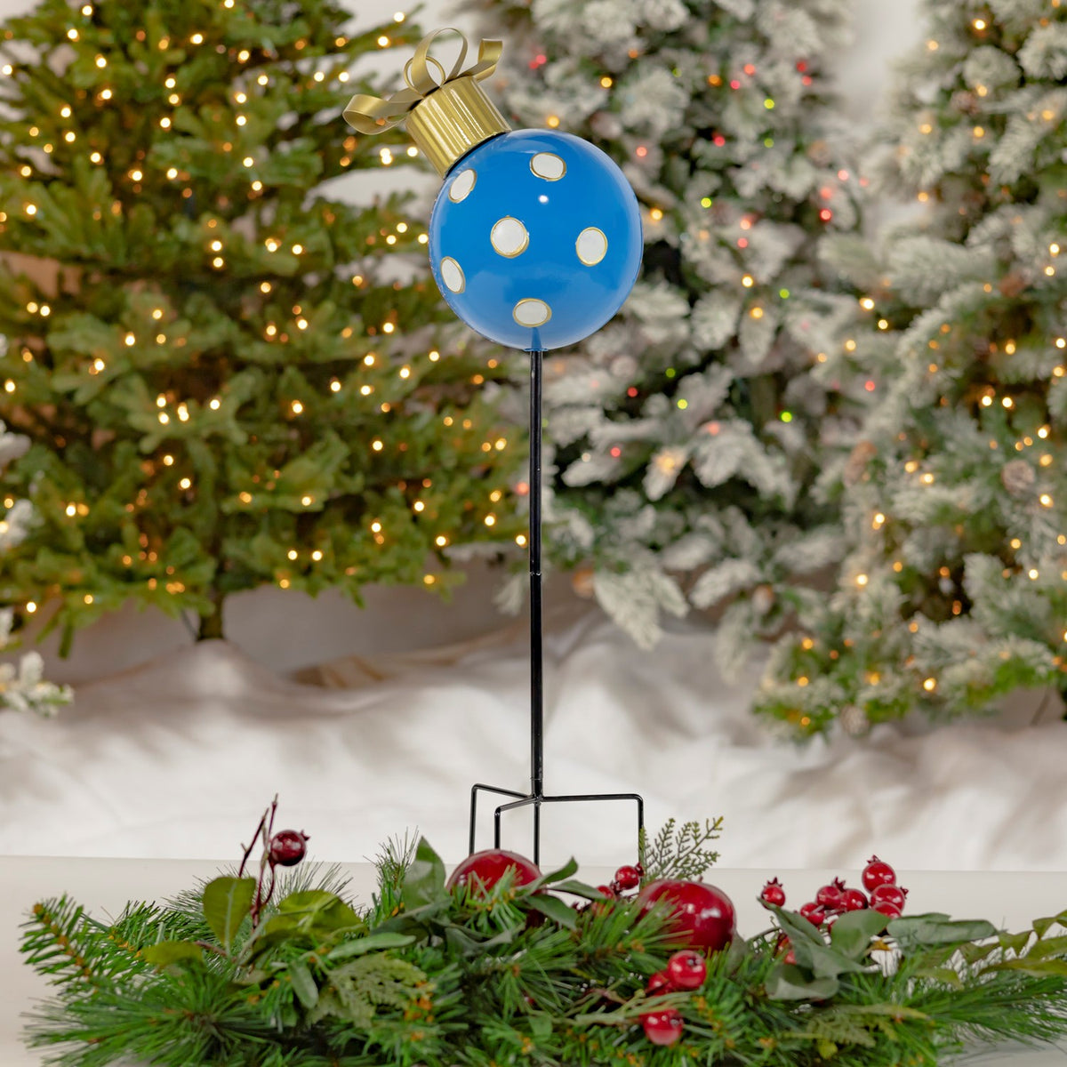 Blue ornament garden stake with white and gold dots set among evergreen greenery and red berries