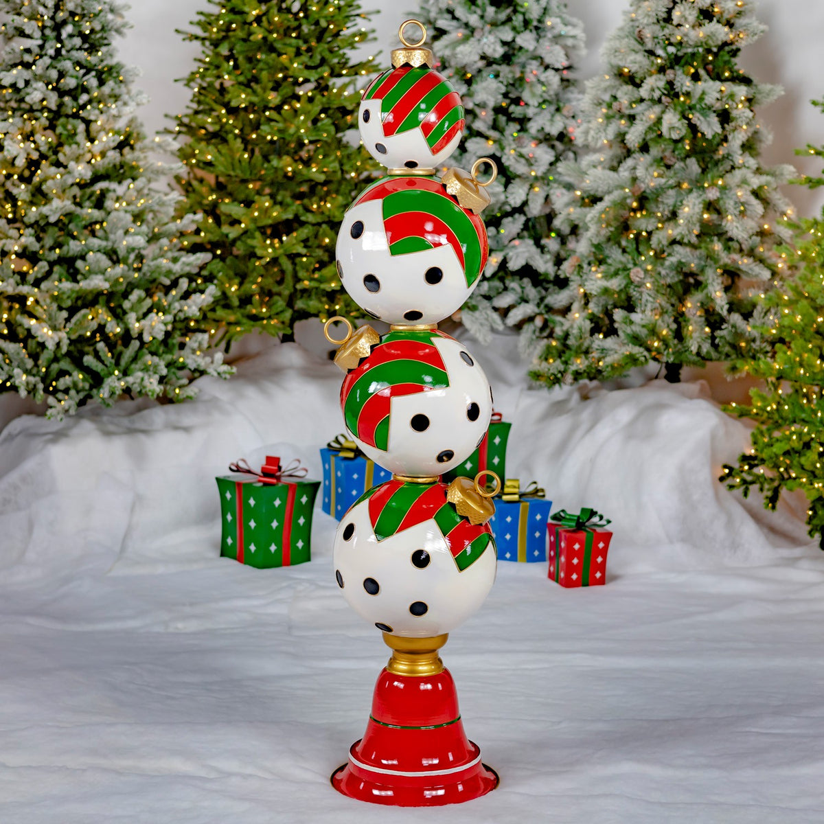 A tower of four white ornaments with black dots and red-and-green stripes on a red base, among Christmas trees and gifts.