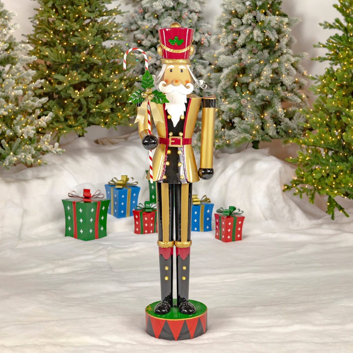 Full-length gold-and-black nutcracker holding a candy cane, posed among lit Christmas trees and wrapped gifts.