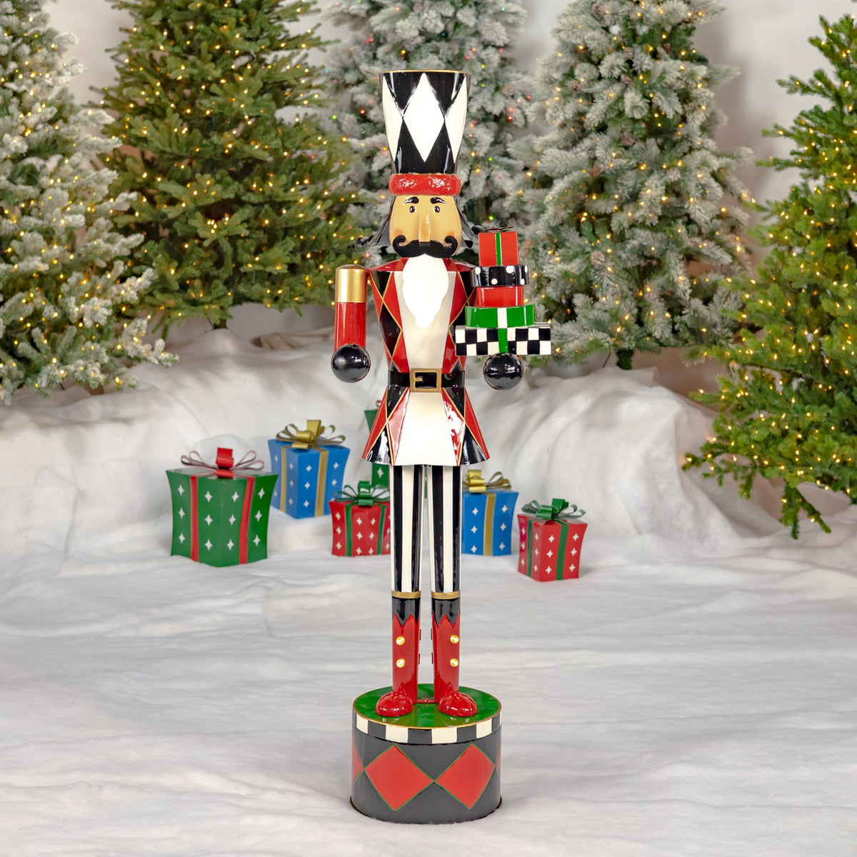 A colorful nutcracker holding wrapped gifts stands on a patterned base among snowy Christmas trees and presents.