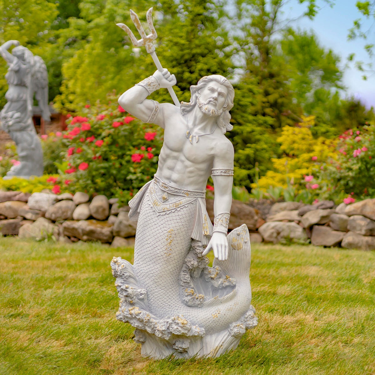 Pale merman statue raises a trident among grass, flowers, and stone edging.