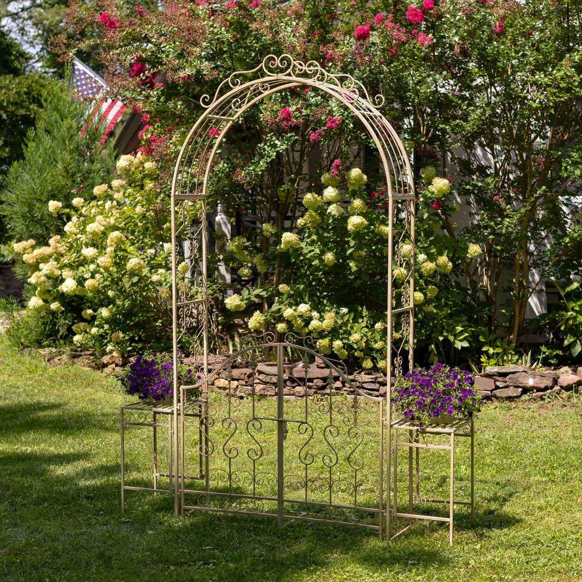 Antique-finish iron garden gate archway with side plant stands in a flower-filled garden