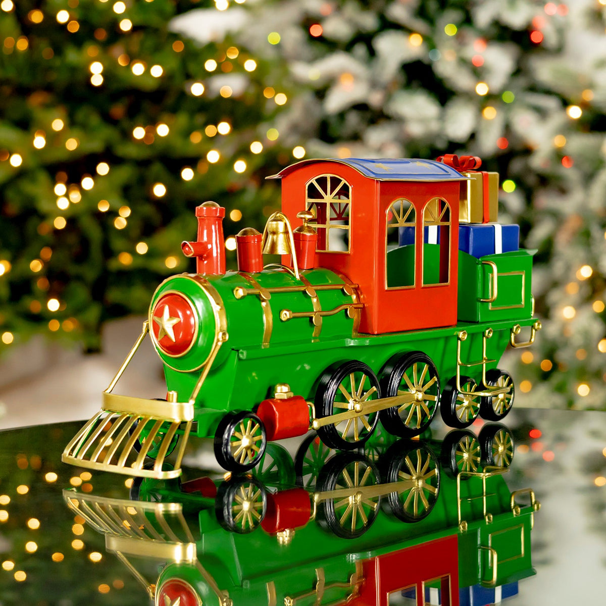 Colorful iron Christmas train displayed on a reflective surface before a lit tree