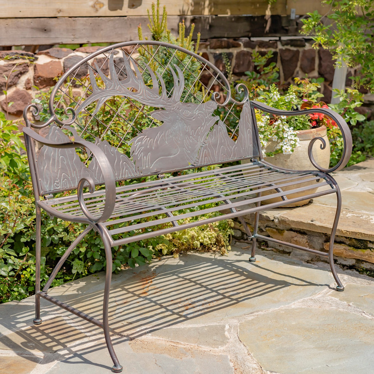 Ornate iron garden bench with a slatted seat and carved caribou backrest on a stone patio